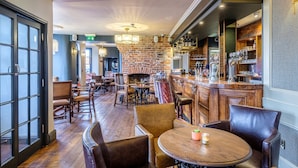 A bar area with wooden furniture, a brick wall, and a bar counter with bottles and glasses. - The Globe Inn Wells (Wells-next-the-Sea)