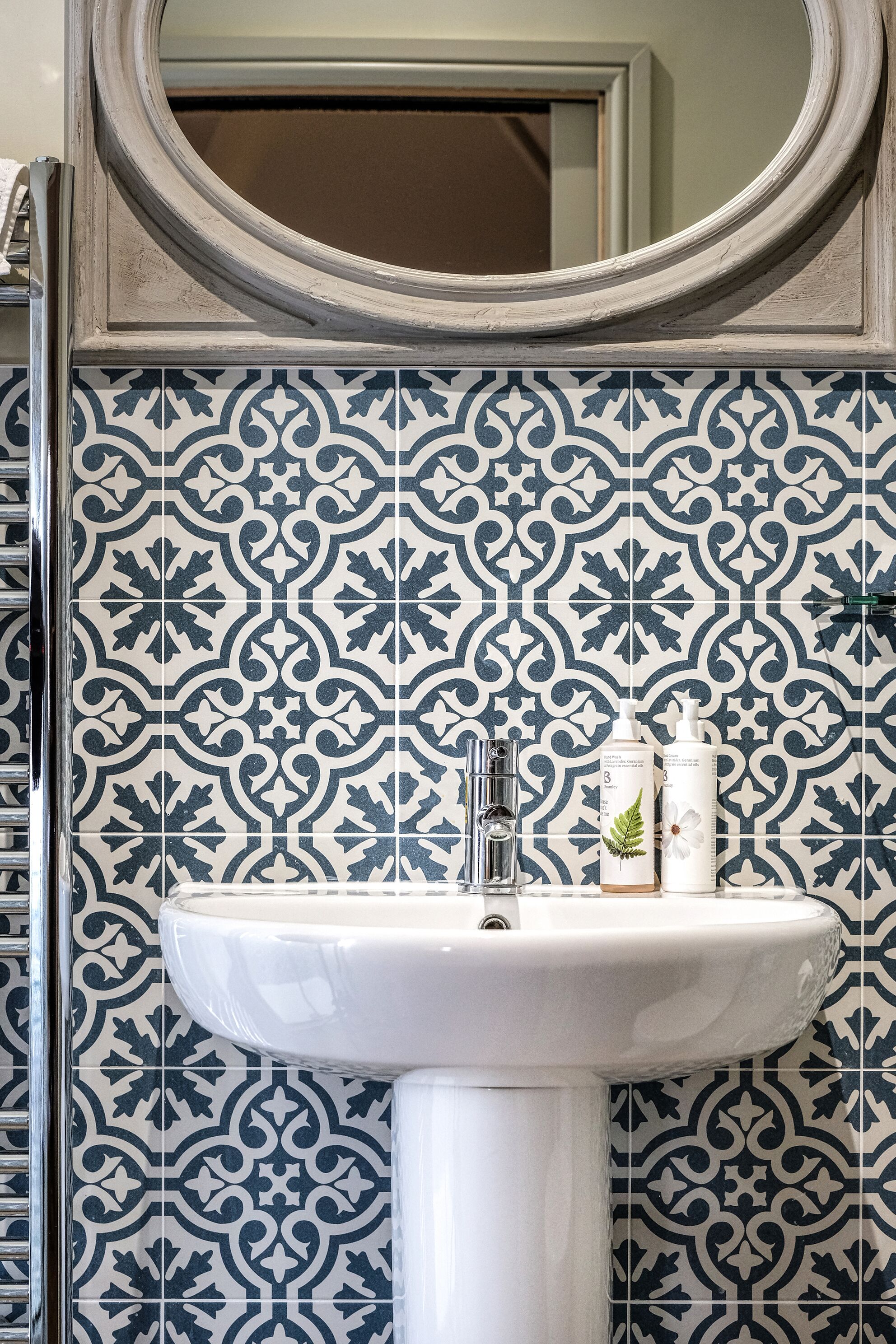A bathroom with a white sink, a mirror, and patterned tiles.