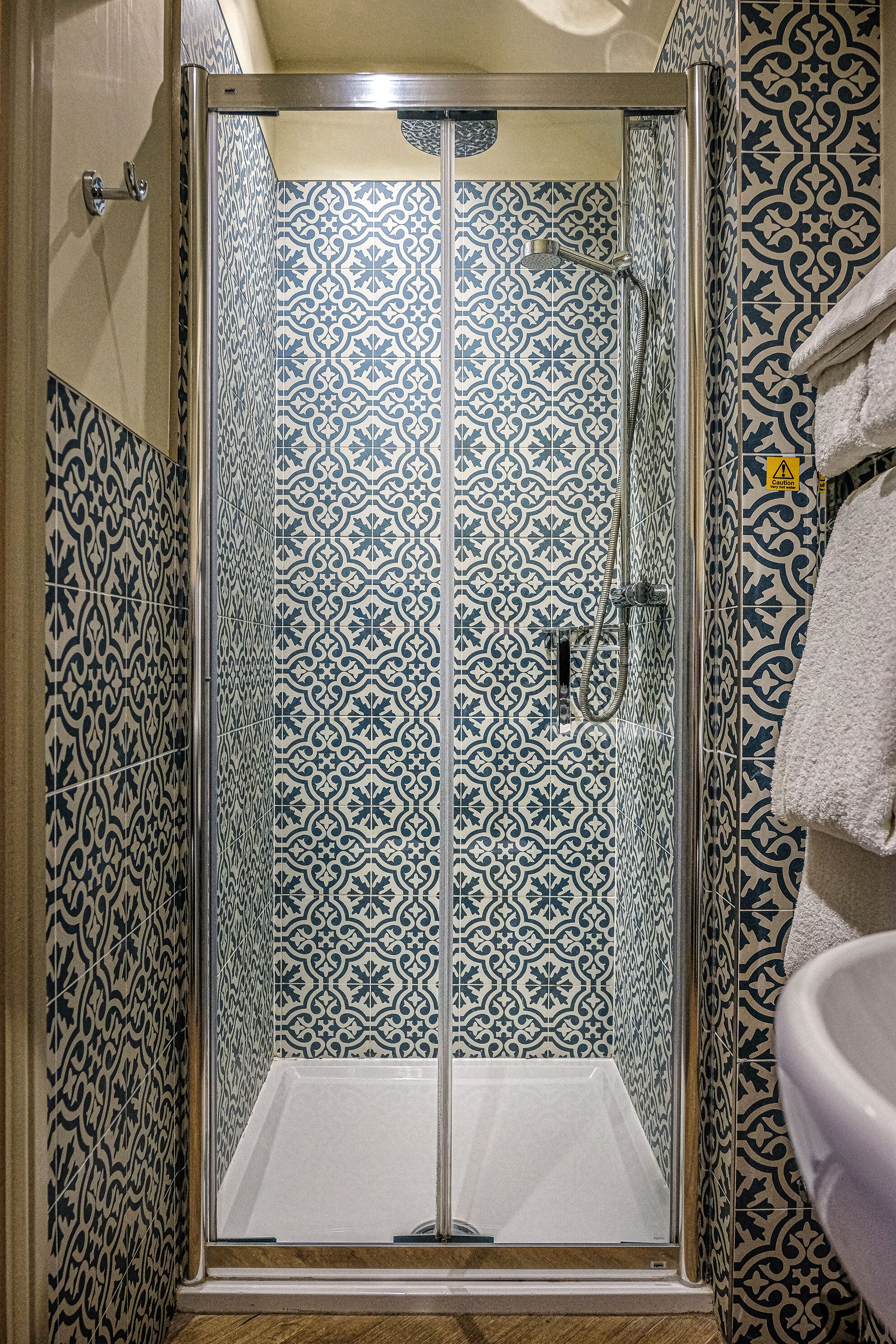 Een douche met een glazen deur, betegelde wanden en een handdoek aan de muur.