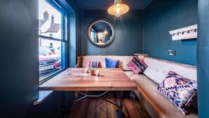 A cozy room with a wooden table, a round mirror, and a bench with cushions. - The Globe Inn Wells (Wells-next-the-Sea)