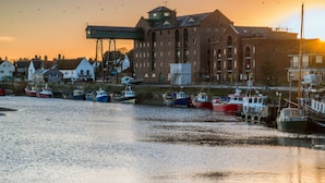 A harbor with boats docked, a large brick building, and a sunset in the background. - The Globe Inn Wells (Wells-next-the-Sea)
