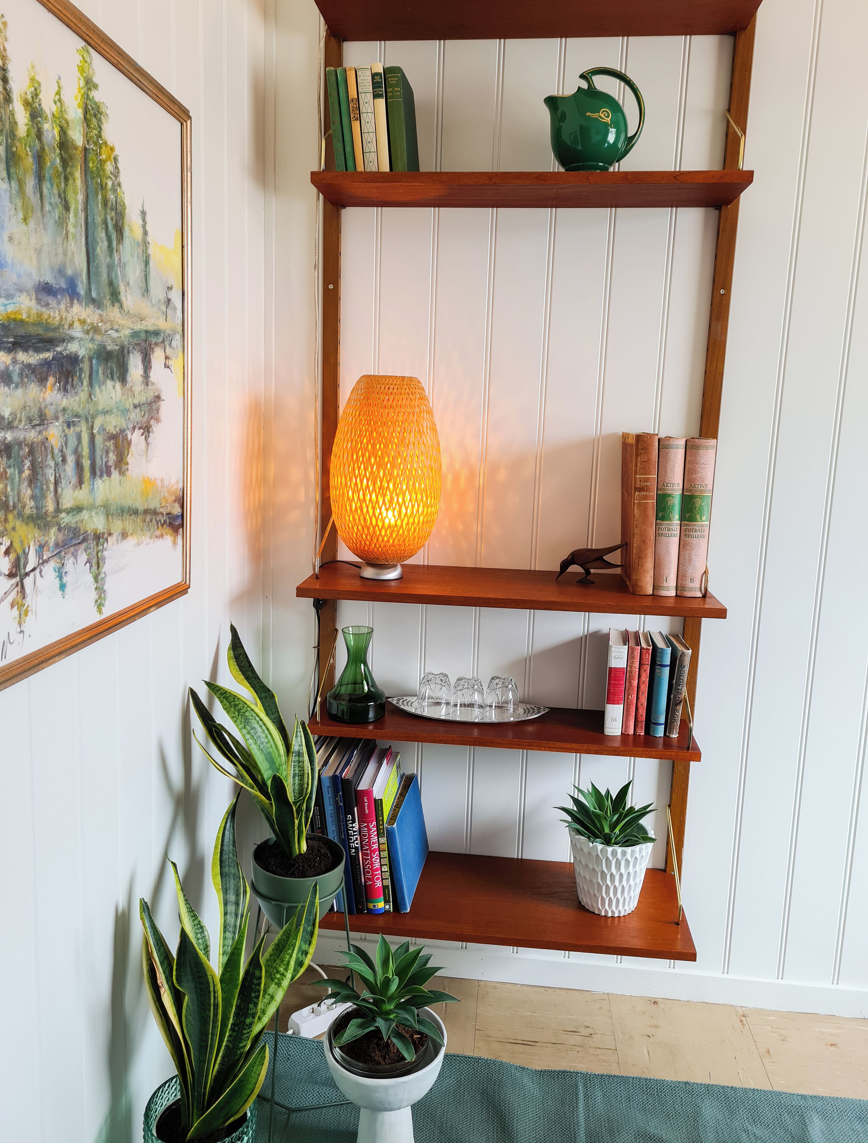A wooden bookshelf with books, a green vase, and a lit orange lamp.