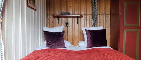 Una cama con una cubierta roja texturizada, dos almohadas blancas y dos almohadas moradas oscuras.