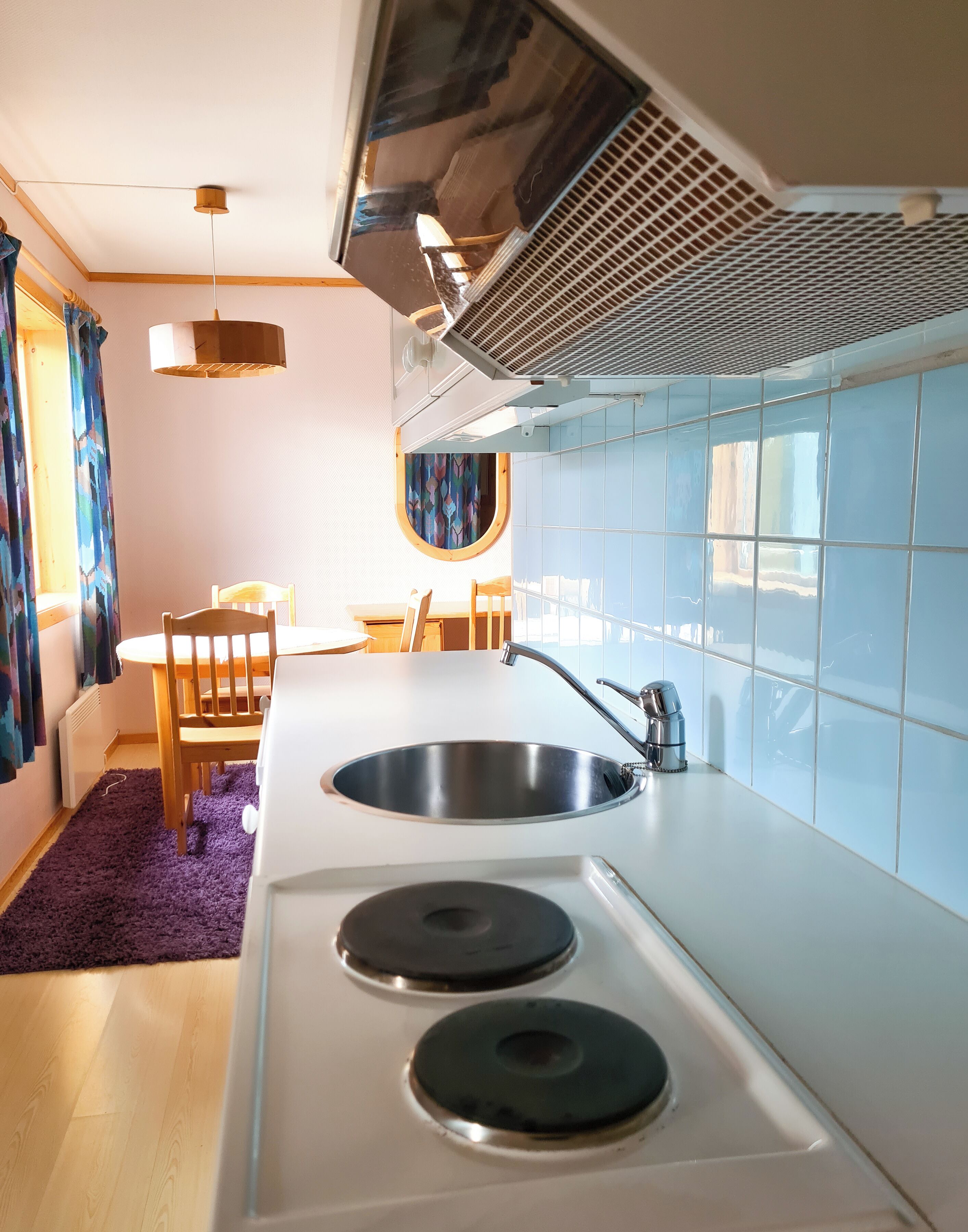 Une cuisine moderne dotée d’un évier en acier inoxydable, de deux plaques de cuisson et d’une fenêtre avec des murs recouverts de carreaux bleus.