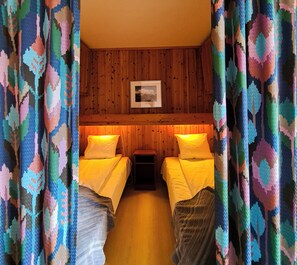 A room with two beds, wooden panel walls, and colorful curtains. - Vauldalen Fjellhotell (Roros)
