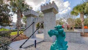 Un parque con una estatua de dragón, un arco de piedra y palmeras.