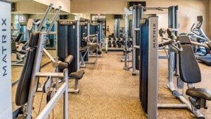 Un gimnasio con diversas máquinas de ejercicio, incluyendo cintas de correr y bancos de pesas, dispuestas en filas.