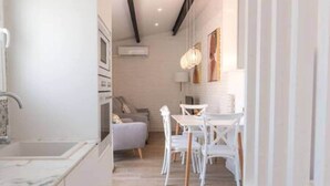 A narrow hallway with a kitchen area on the left, a dining table with chairs in the center, and a sofa in the background. - Blanda Family Apartment (Blanes)