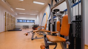 Een sportschool met trainingsapparatuur, een tv aan de muur en een houten vloer.