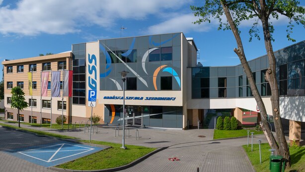 Een modern gebouw met een glazen gevel, een parkeerbord en een symbool voor rolstoeltoegankelijkheid.