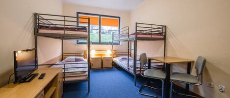 A dormitory room with bunk beds, a desk with a computer, a chair, and a small table.