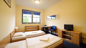 Een hotelkamer met twee eenpersoonsbedden, een bureau met stoel, een televisie en een raam met uitzicht op gebouwen.