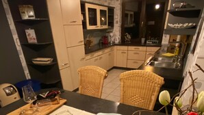 A modern kitchen with dark countertops, white cabinets, and a central island with a fish-shaped bowl. There are wicker chairs around the island and a vase with tulips on the right. - Vacation apartment Pier 7 - directly on the lake! (Bitterfeld-Wolfen)