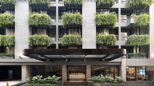 Un edificio moderno con varios balcones decorados con follaje, un acceso cubierto y un área exterior bien cuidada con escalones que conducen a la entrada.