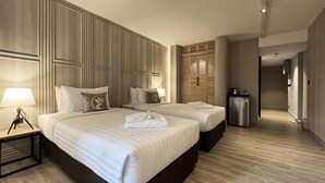 Una habitación de hotel con dos camas, una mesita de noche con lámpara, un minibar y un armario de madera.