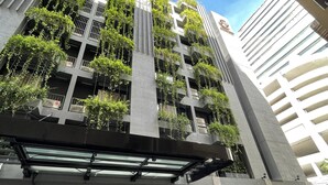 Un edificio moderno con varios balcones cubiertos de vegetación, ventanas amplias y una zona de entrada bien iluminada con escalones que conducen a la puerta.