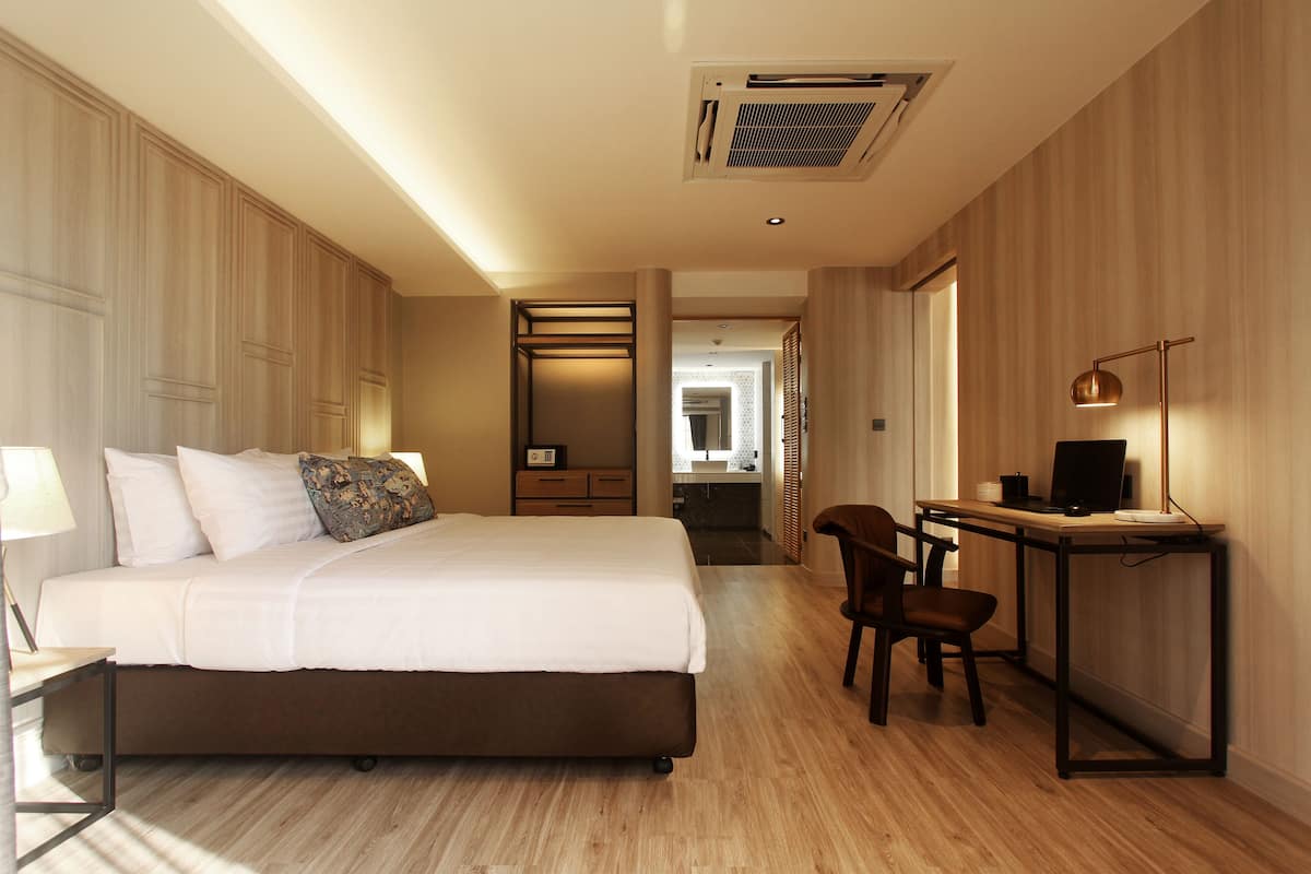 Habitación de hotel con cama, escritorio, silla, lámpara y vista al baño.