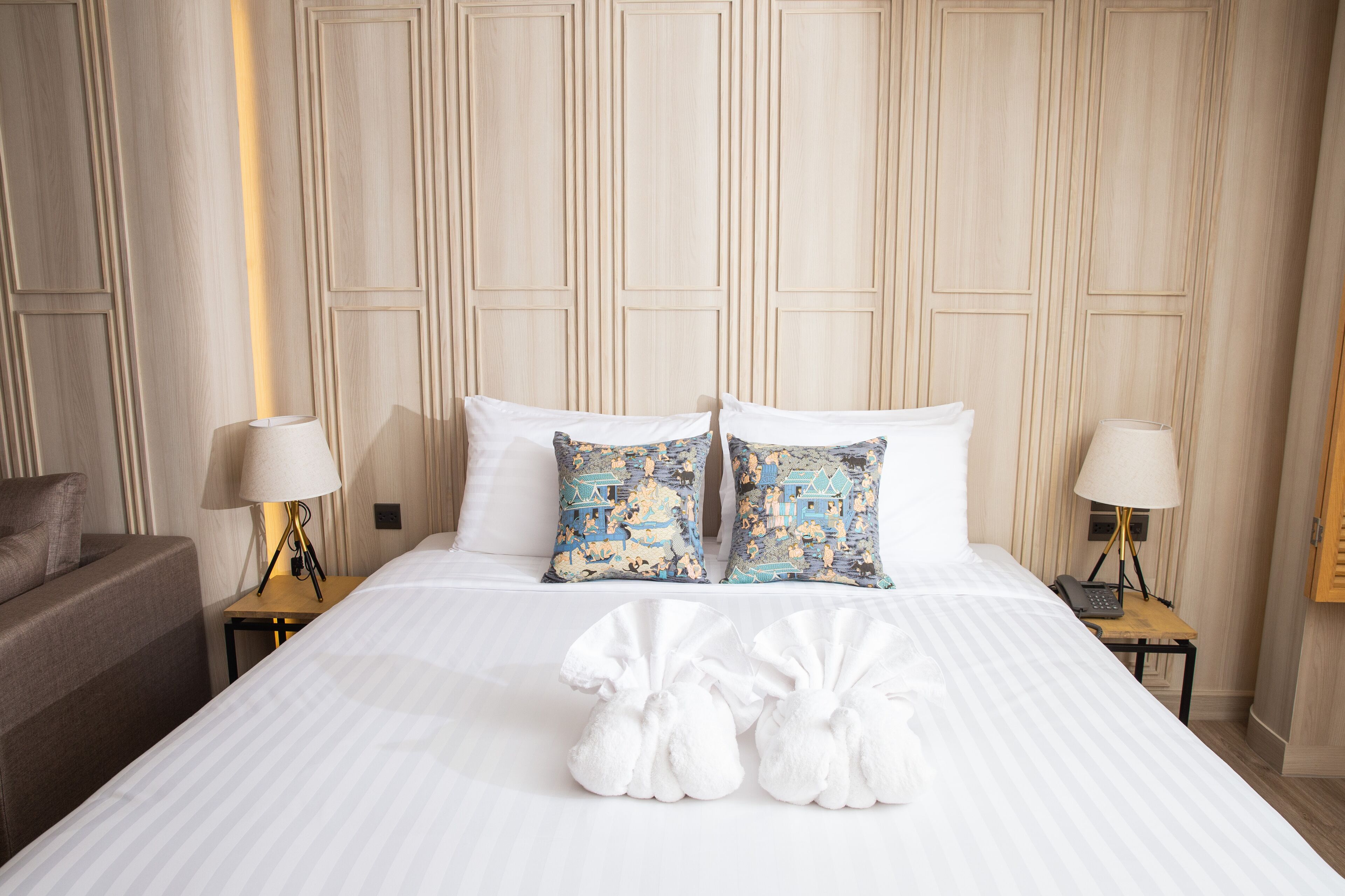 A hotel room with a large bed, two pillows, a bedside table with a lamp, and a chair.