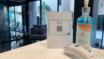 Un dispensador de gel hidroalcohólico, un código QR y una caja sobre una mesa en una habitación moderna con ventanales amplios.
