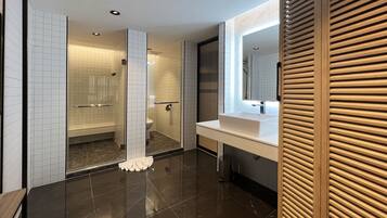 A modern bathroom with a glass shower enclosure, a vanity with a large mirror, and a tiled floor.