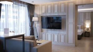 Una moderna camera d'albergo con televisione a schermo piatto fissata al muro, un divano, un tavolino e un letto con un comodino.