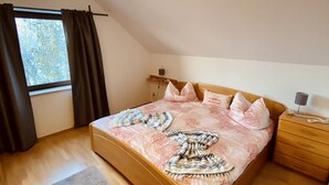 A bedroom with a wooden bed, a nightstand, a bedside lamp, a window with curtains, and a ceiling light.