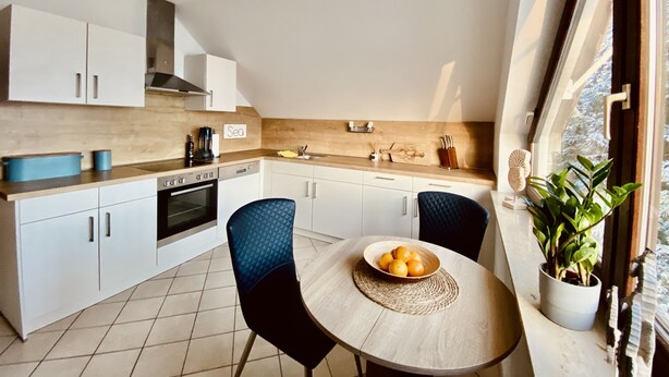 A modern kitchen with white cabinets, a wooden countertop, and a dining table with chairs.