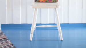 Une chaise blanche avec un coussin coloré, placée contre un mur blanc et sur un sol bleu.