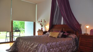 A bedroom with a bed, a nightstand, a lamp, and a window with a view of greenery.