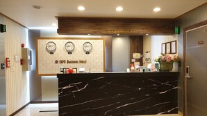 A reception desk with a marble top, clocks displaying New York, London, and Seoul times, and a sign for OKPD Business Hotel. - Okpo Business Hotel (Geoje)