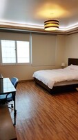 A hotel room with a bed, a desk, a chair, a lamp, and a window.