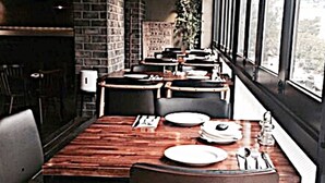 A restaurant with a long wooden table, black chairs, and hanging pendant lights. - Okpo Business Hotel (Geoje)