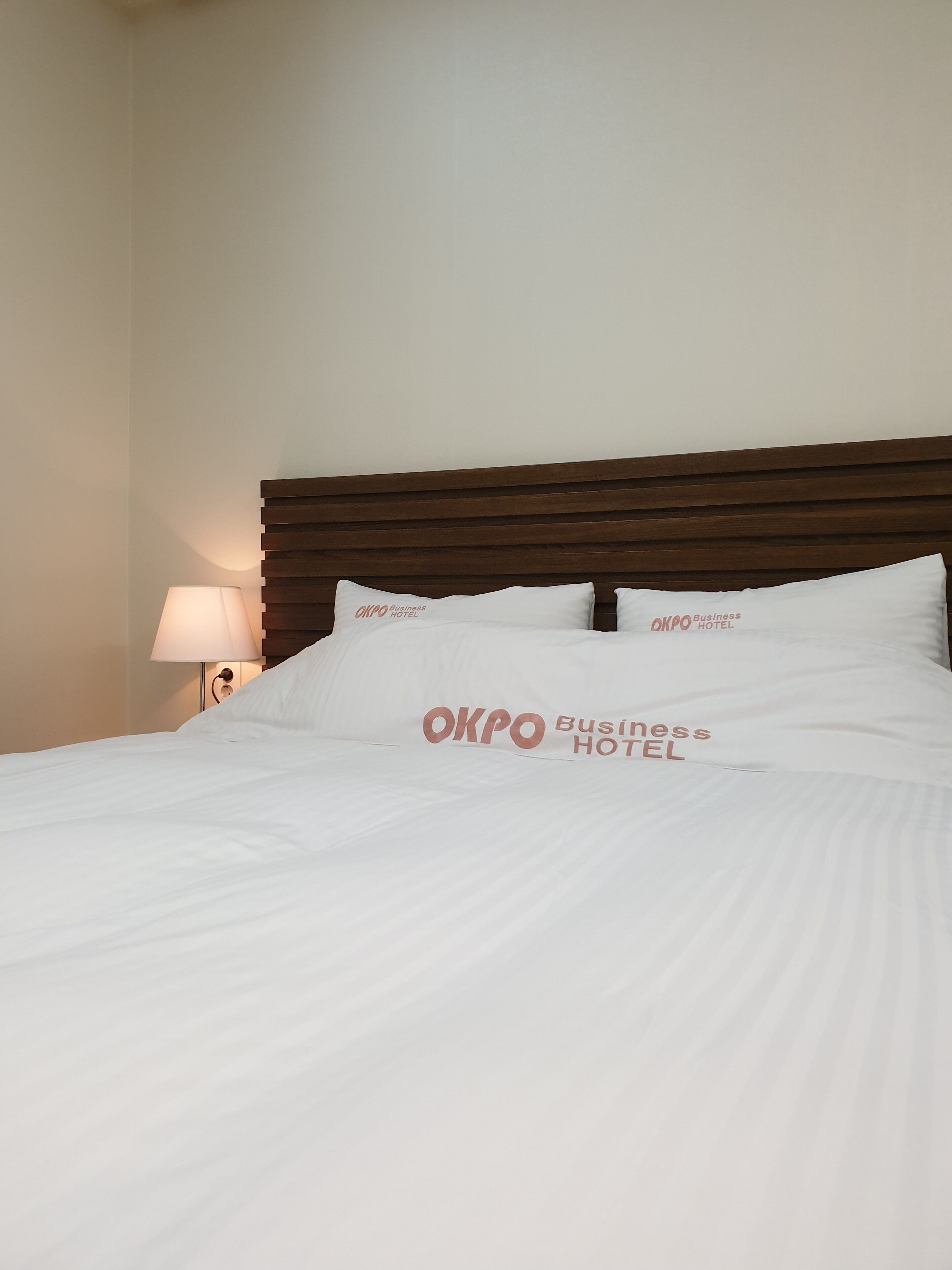 A hotel room with a neatly made bed, a wooden headboard, and pillows with the hotel name.