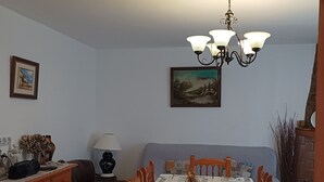 A dining area with a table set for four, a chandelier, a painting on the wall, and a cabinet with decorative items. - RURAL HOUSE IDEAL FOR CELEBRATIONS, LARGE LIVING ROOM, BARBECUE, 18 PEOPLE (Valdemoro-Sierra)