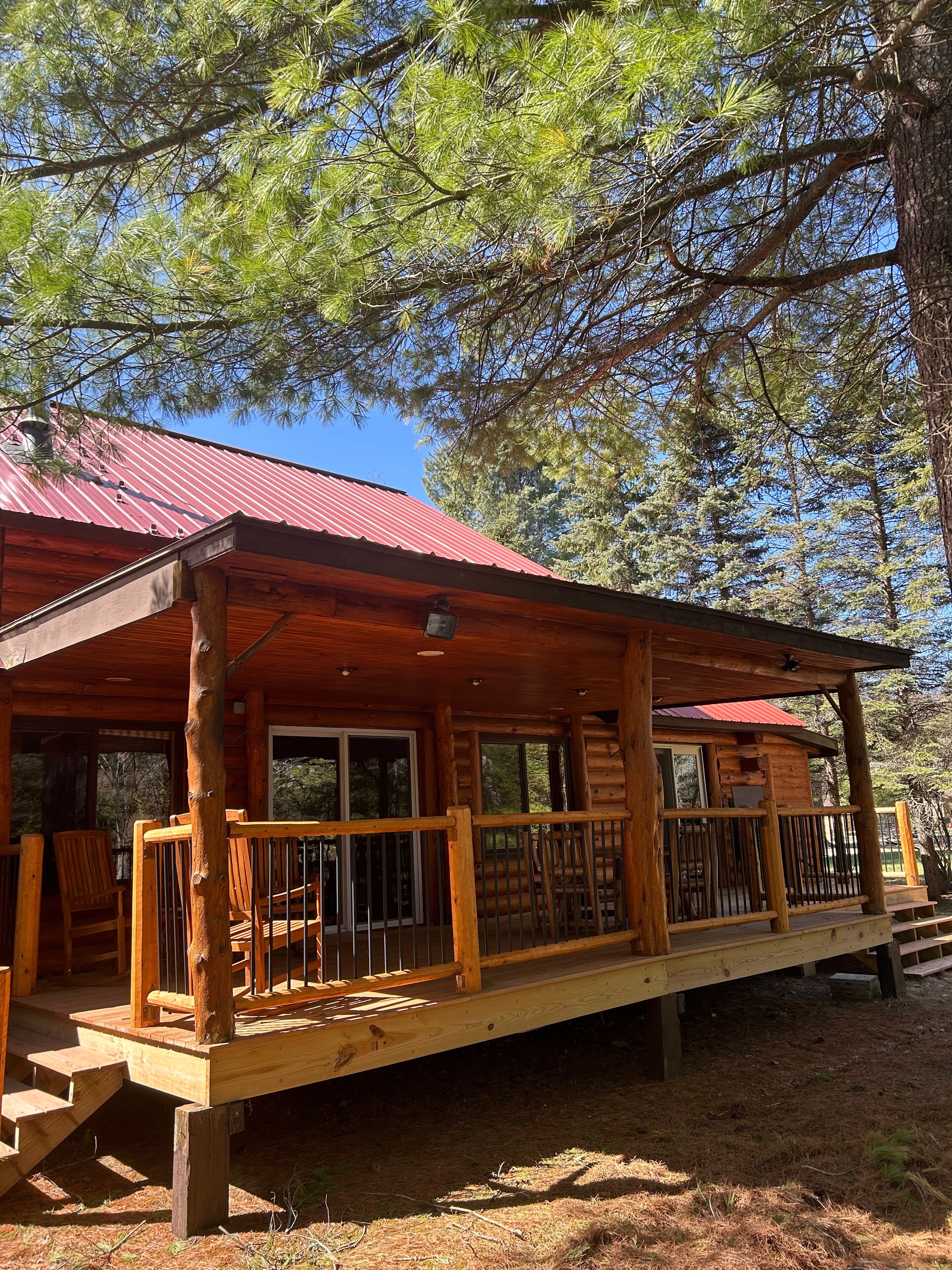 A wooden cabin with a red roof, a covered porch with wooden railings, and a staircase leading to the entrance.