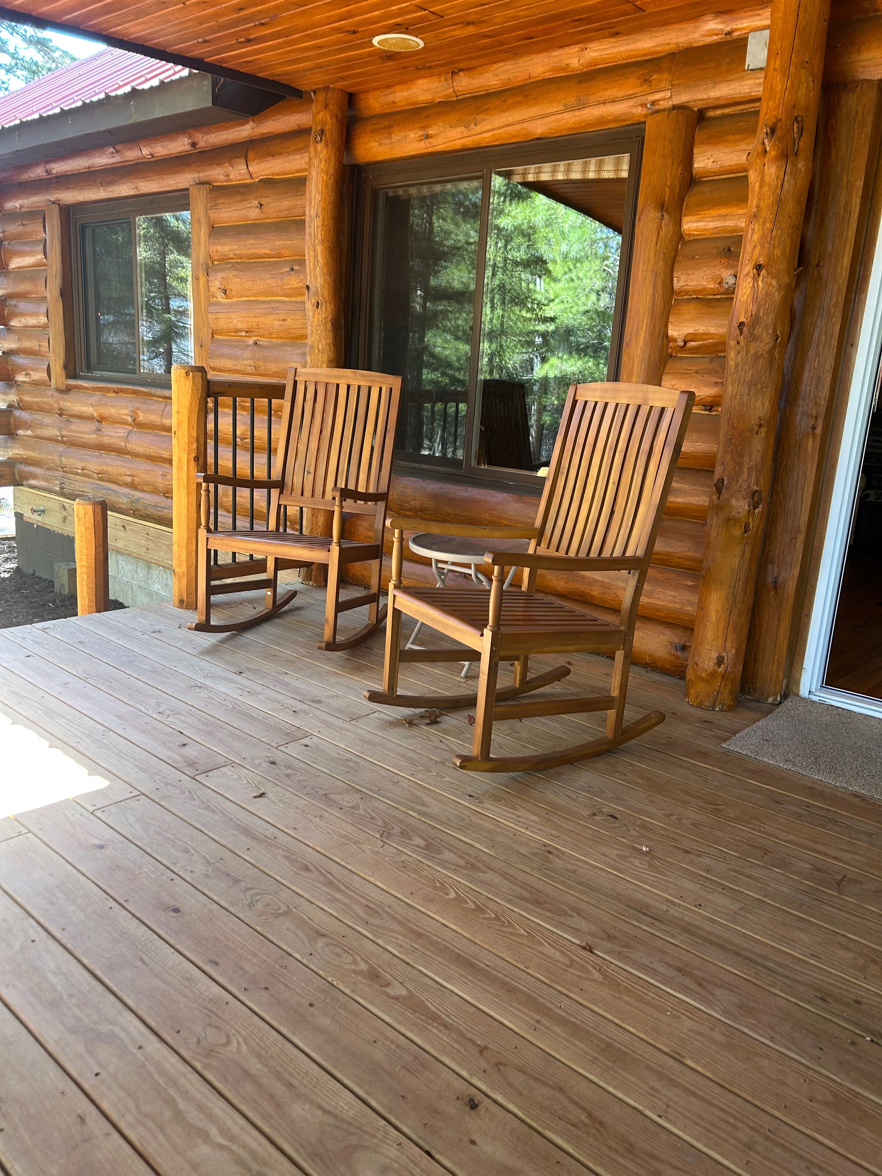A wooden log cabin with a porch featuring two rocking chairs and a small table.