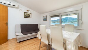 A room with a sofa, dining table, chairs, and a view of a mountainous landscape through a window. - Apartments Fran (Vela Luka)