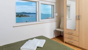 A bedroom with a bed, a chair, a wardrobe, and a window with a view of the sea. - Apartments Fran (Vela Luka)