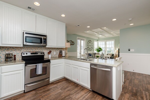 A modern kitchen with white cabinetry, stainless steel appliances, and a wooden floor. - Book 'Walk to the Beach,’ a Classic 1-BR Condo@Cinnamon Shore w/ Amenities! (Port Aransas)