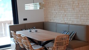 Uma sala de jantar com mesa de madeira, cadeiras de vime, um banco acolchoado e teto com vigas aparentes.