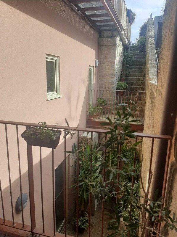 A narrow alleyway with a pink building, a metal railing, and potted plants.