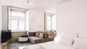 A bedroom with a bed, a sofa, a TV, and a small table with a lamp. - ORM - Almada Apartments (Porto)