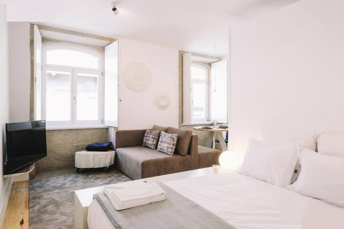 A bedroom with a bed, a sofa, a TV, and a small table with a lamp.
