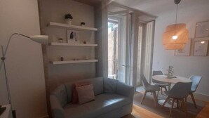 A modern living room with a grey sofa, white shelves, a dining table with chairs, and a checkered rug. - ORM - Almada Apartments (Porto)