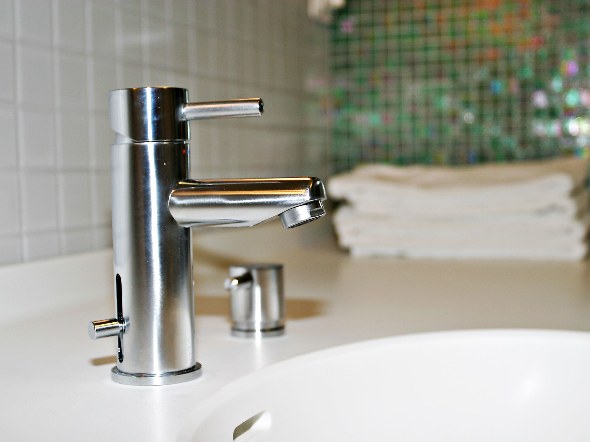 A modern bathroom with a chrome faucet, a white sink, and a tiled backsplash.