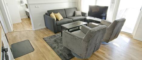 Una sala moderna con un sofá gris, un sillón estampado y una mesa de centro de vidrio.
