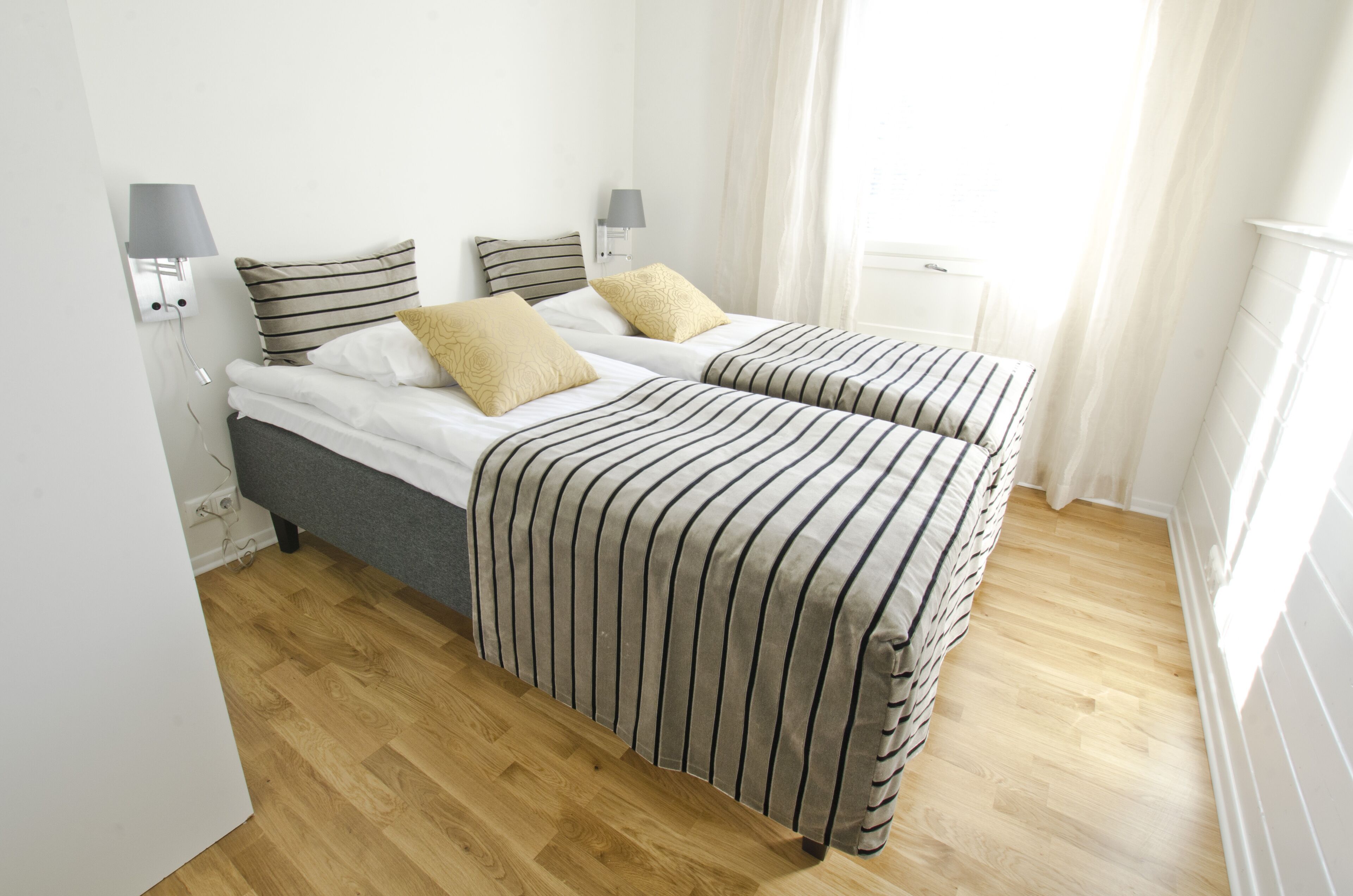 A bedroom with two beds, a wooden floor, and a window with curtains.