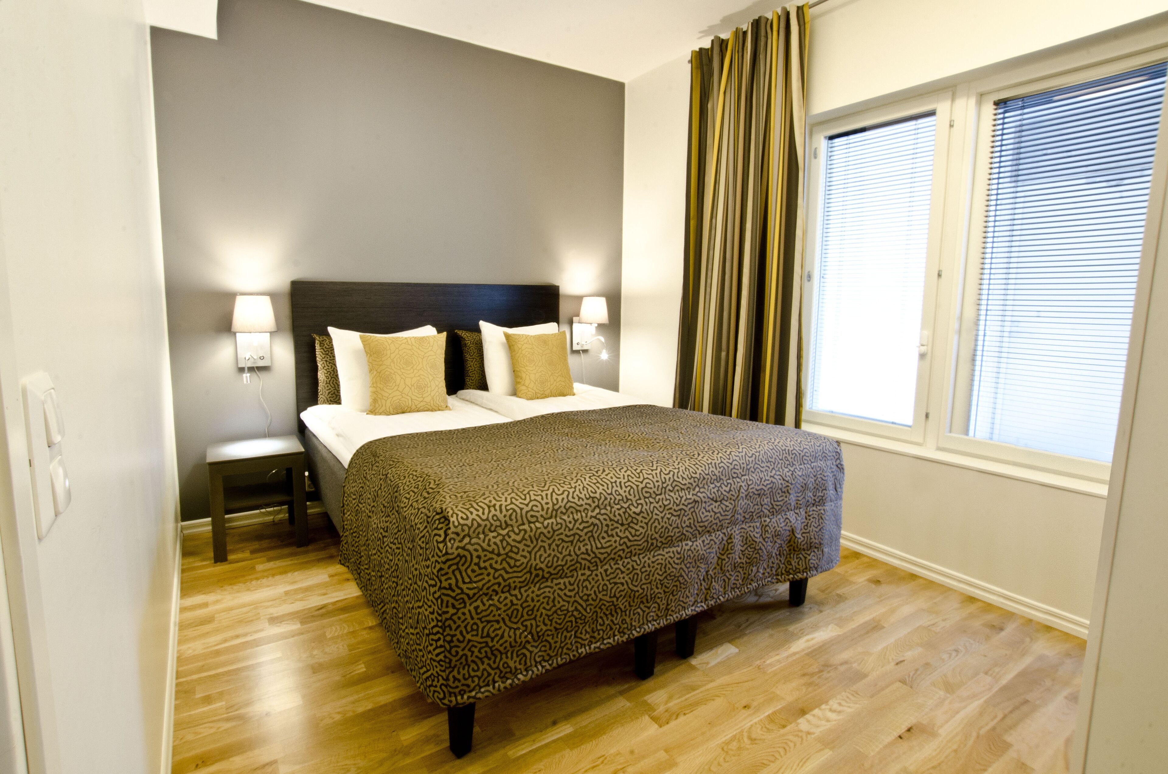 A bedroom with a bed, two bedside tables, a window with blinds, and a curtain.