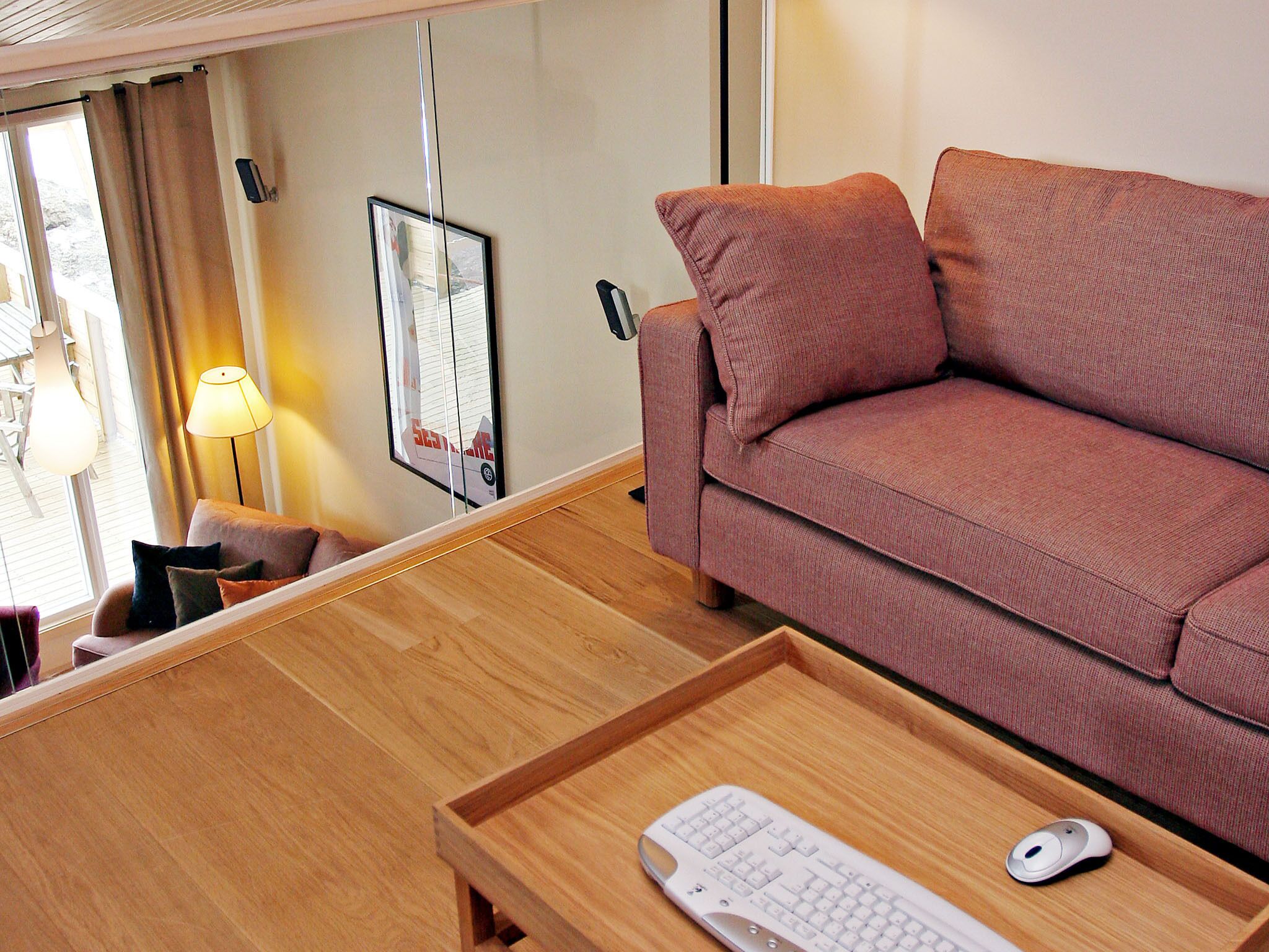 A room with a wooden desk, a pink sofa, a white keyboard, and a mouse on the desk.