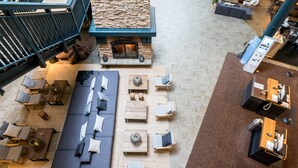 A spacious lounge area with a long dark-colored sofa, multiple small tables, and chairs arranged for socializing. A stone fireplace adds a focal point to the space.